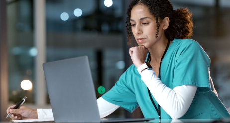Doctora con uniforme verde trabajando en ordenador portátil y tomando notas en oficina médica