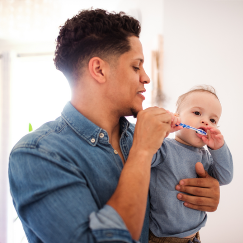 Padre cepillando los dientes de su bebé mientras lo sostiene en brazos.