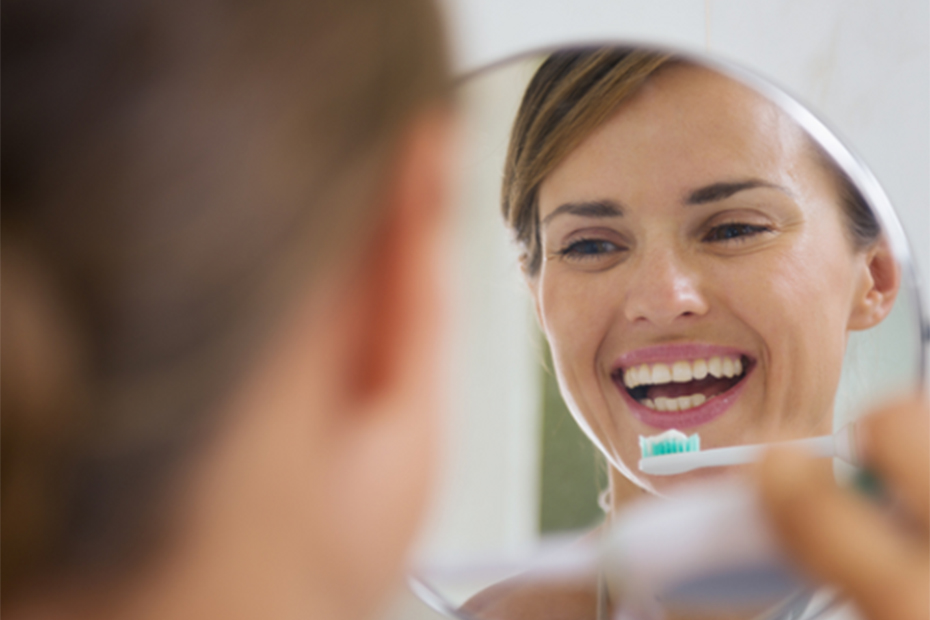 Mujer sonriente cepillándose los dientes frente al espejo