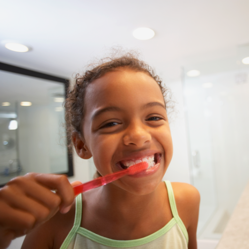 Niña cepillandose los dientes frente al espejo